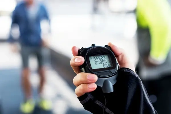 A handheld stopwatch in focus, with people blurred in the background.